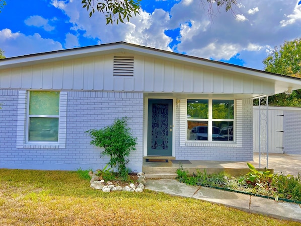 A single-story house with a front door, two windows, and a small tree in the front yard.