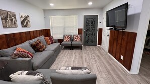 Un salon moderne avec un canapé gris, des coussins à motifs, un fauteuil gris et un téléviseur à écran plat fixé au mur.