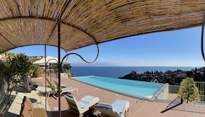 Uma área à beira da piscina com espreguiçadeiras e vista para o mar.