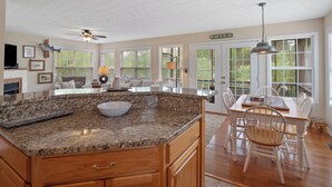Una cocina amplia con encimeras de granito, armarios de madera y un comedor con sillas blancas y una mesa de madera.