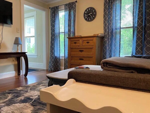 Un dormitorio con cama, cómoda, reloj y ventana con cortinas.