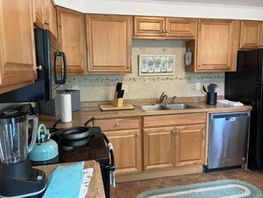 Una cocina con armarios de madera, lavavajillas de acero inoxidable, estufa negra y hervidor azul.