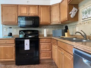 Une cuisine avec des meubles de rangement en bois, une cuisinière noire, un four à micro-ondes et un lave-vaisselle.
