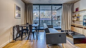 Una sala de estar moderna con sofá, mesa de comedor, sillas y vista a un paisaje urbano a través de amplios ventanales.