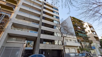 Un edificio de varios pisos con balcones, acceso a garaje y coches estacionados.