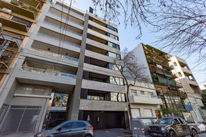 A multi-story building with balconies, a garage entrance, and parked cars.
