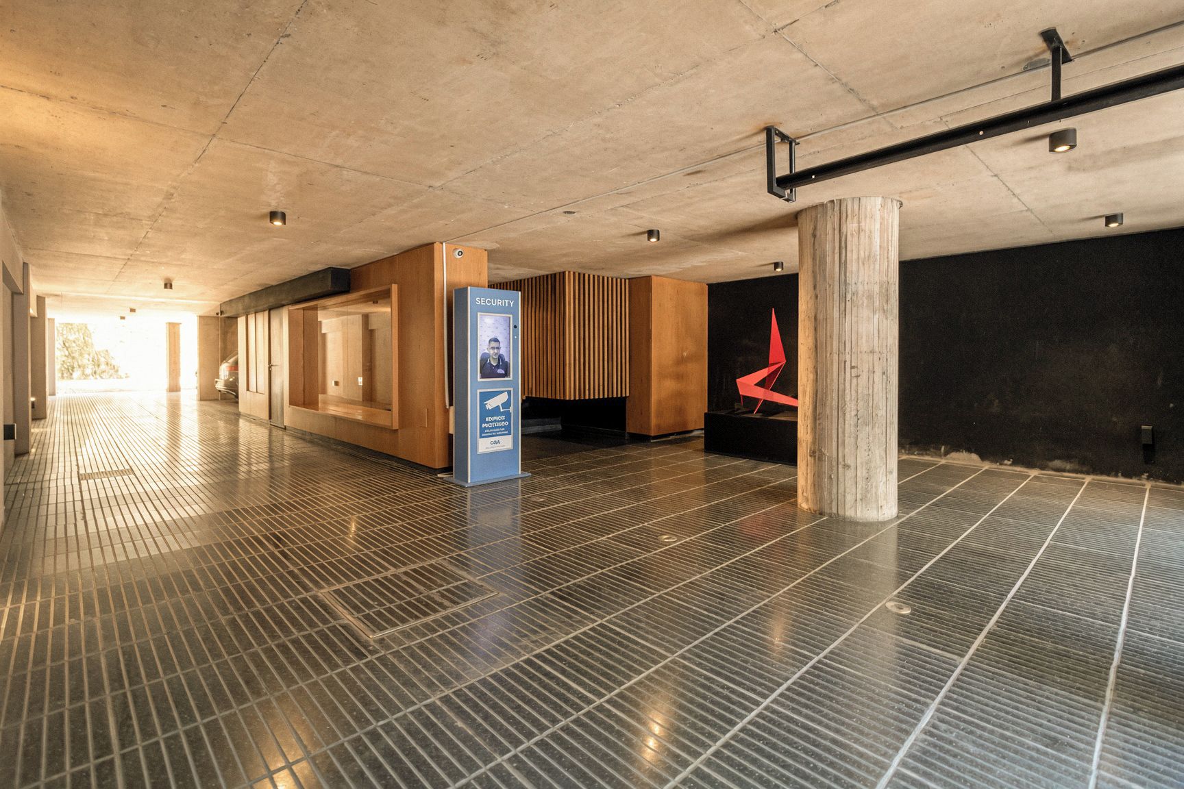 A spacious indoor area with a tiled floor, a security kiosk, and a wooden reception desk.