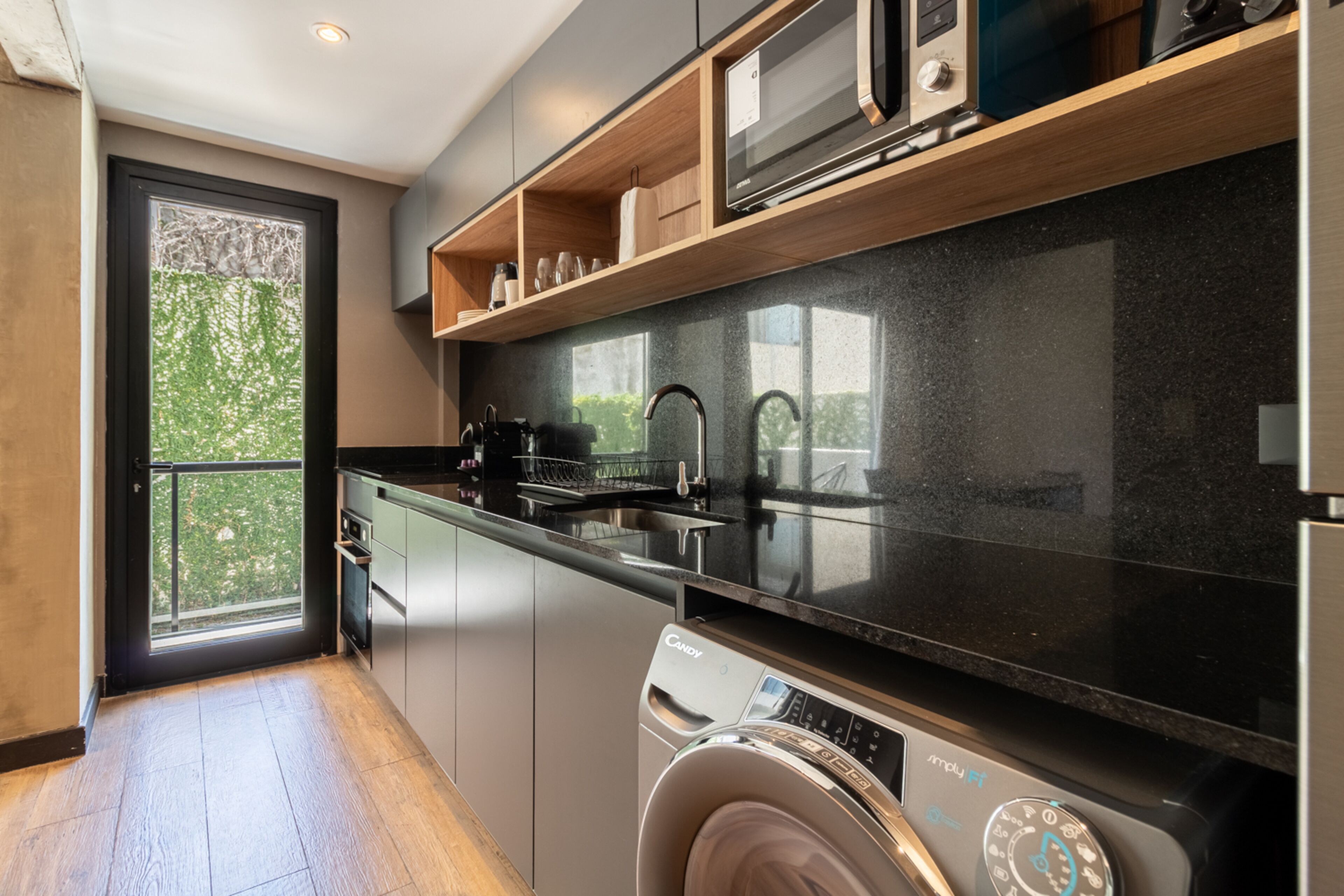 Una cocina moderna con lavadora y secadora integradas, electrodomésticos de acero inoxidable y un amplio ventanal con vistas a zonas verdes.