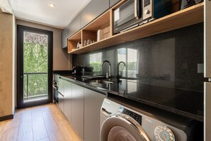 A modern kitchen with a built-in washer and dryer, stainless steel appliances, and a large window offering a view of greenery.