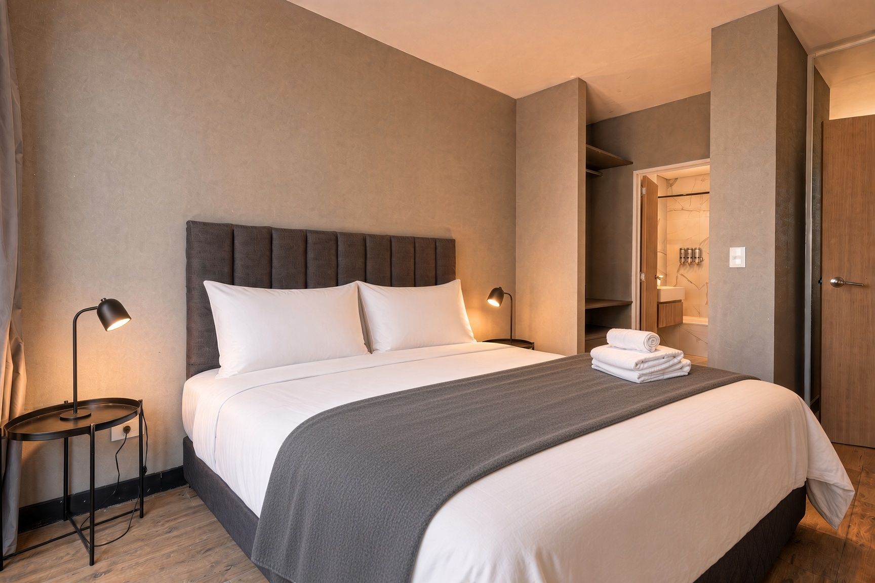 A hotel room with a bed, bedside lamps, a round table, and a bathroom visible through an open door.