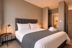 Habitación de hotel con cama, lámparas de noche, una mesa redonda y baño visible a través de una puerta abierta.