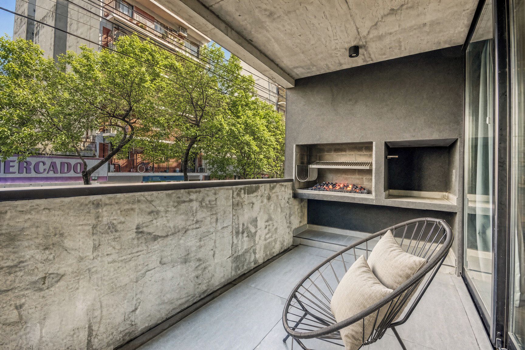 Un balcón con un muro de concreto, una silla de metal y una zona de parrilla.