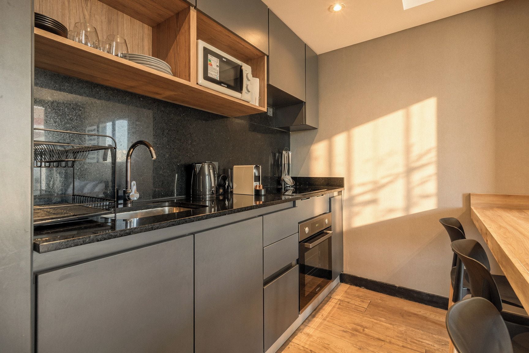 Una cocina moderna con horno integrado, cafetera y microondas sobre una repisa de madera.