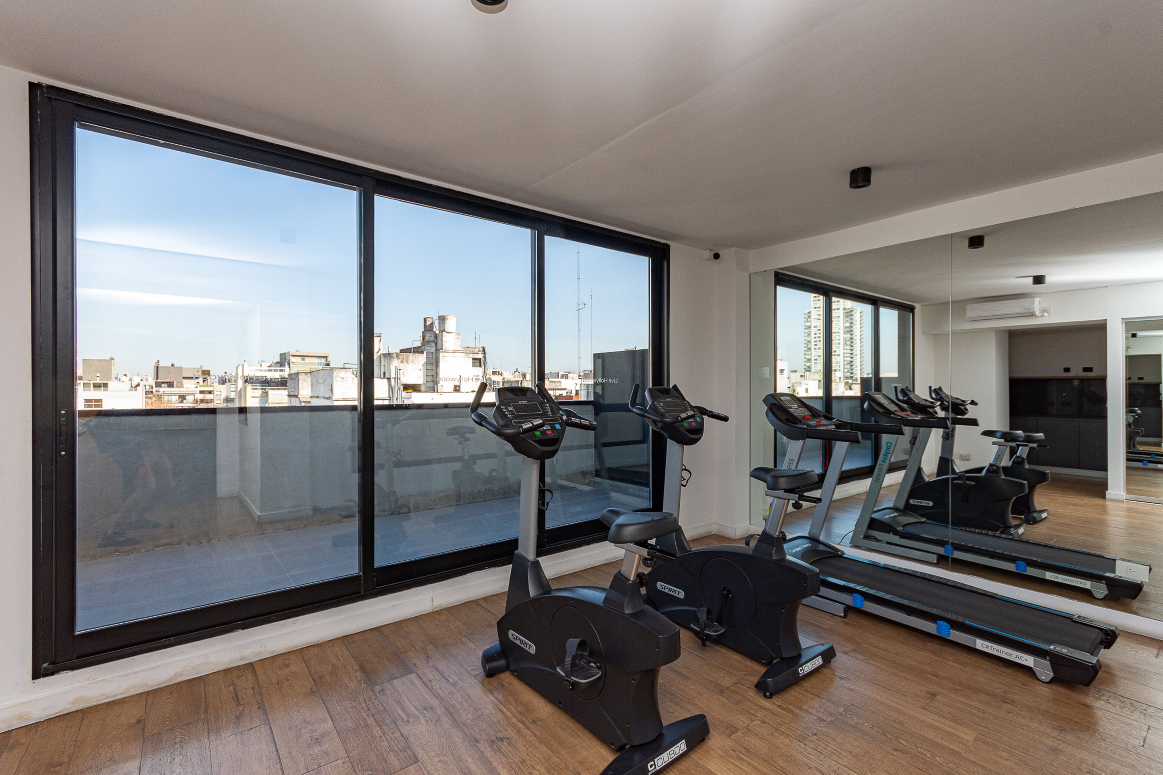 Un gimnasio con equipo de ejercicio y ventanas amplias que ofrecen vistas a la ciudad.