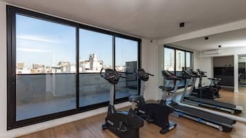 Un gimnasio con equipo de ejercicio y ventanas amplias que ofrecen vistas a la ciudad.