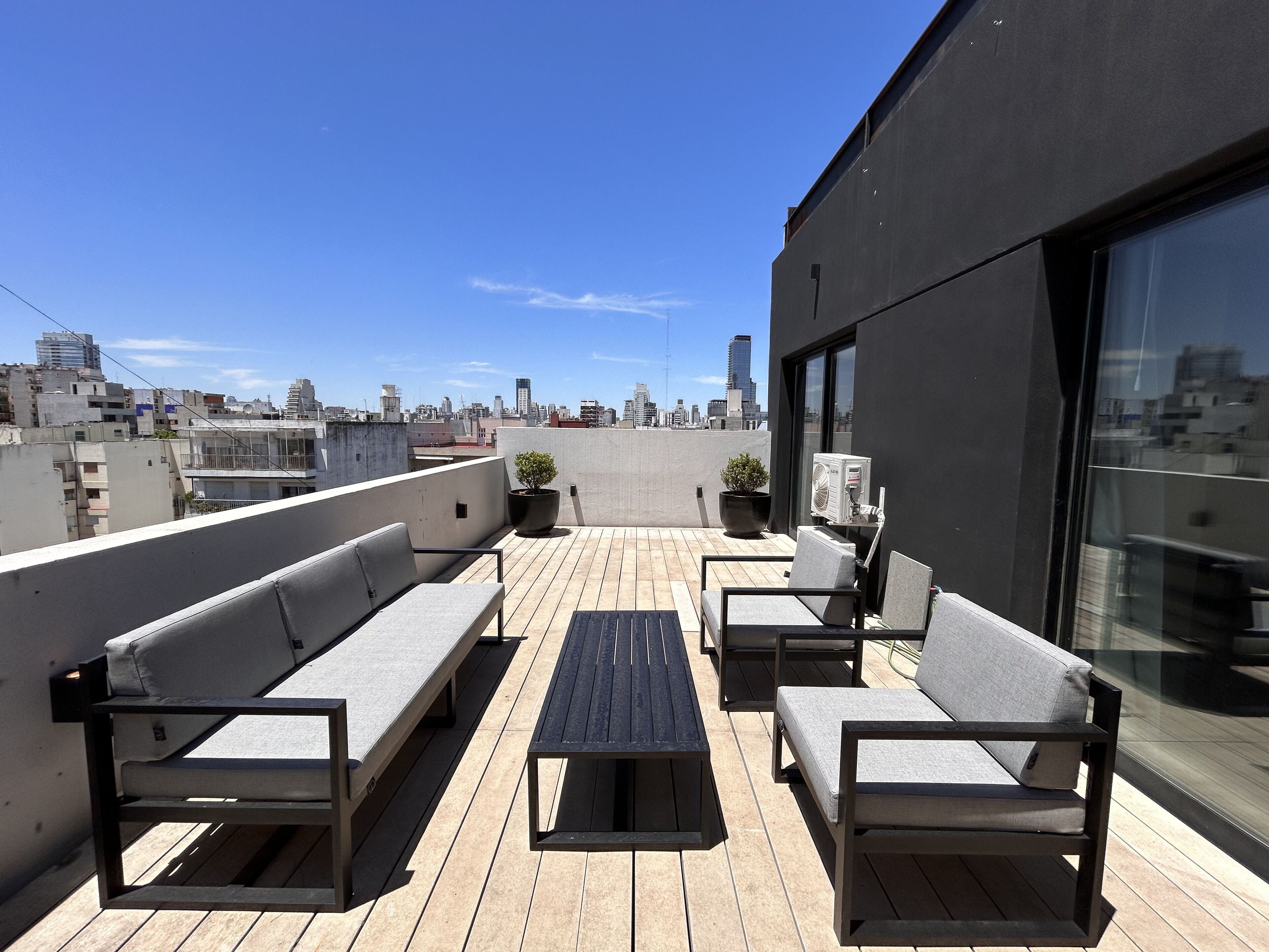 Terraza en la azotea con mobiliario exterior, una planta en maceta y vistas del horizonte urbano.