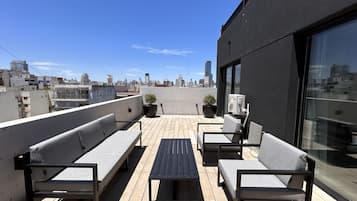 Terraza en la azotea con mobiliario exterior, una planta en maceta y vistas del horizonte urbano.