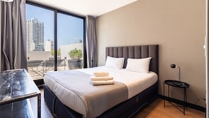 Habitación de hotel moderna con una cama grande, una mesita y vistas a la ciudad por la ventana.
