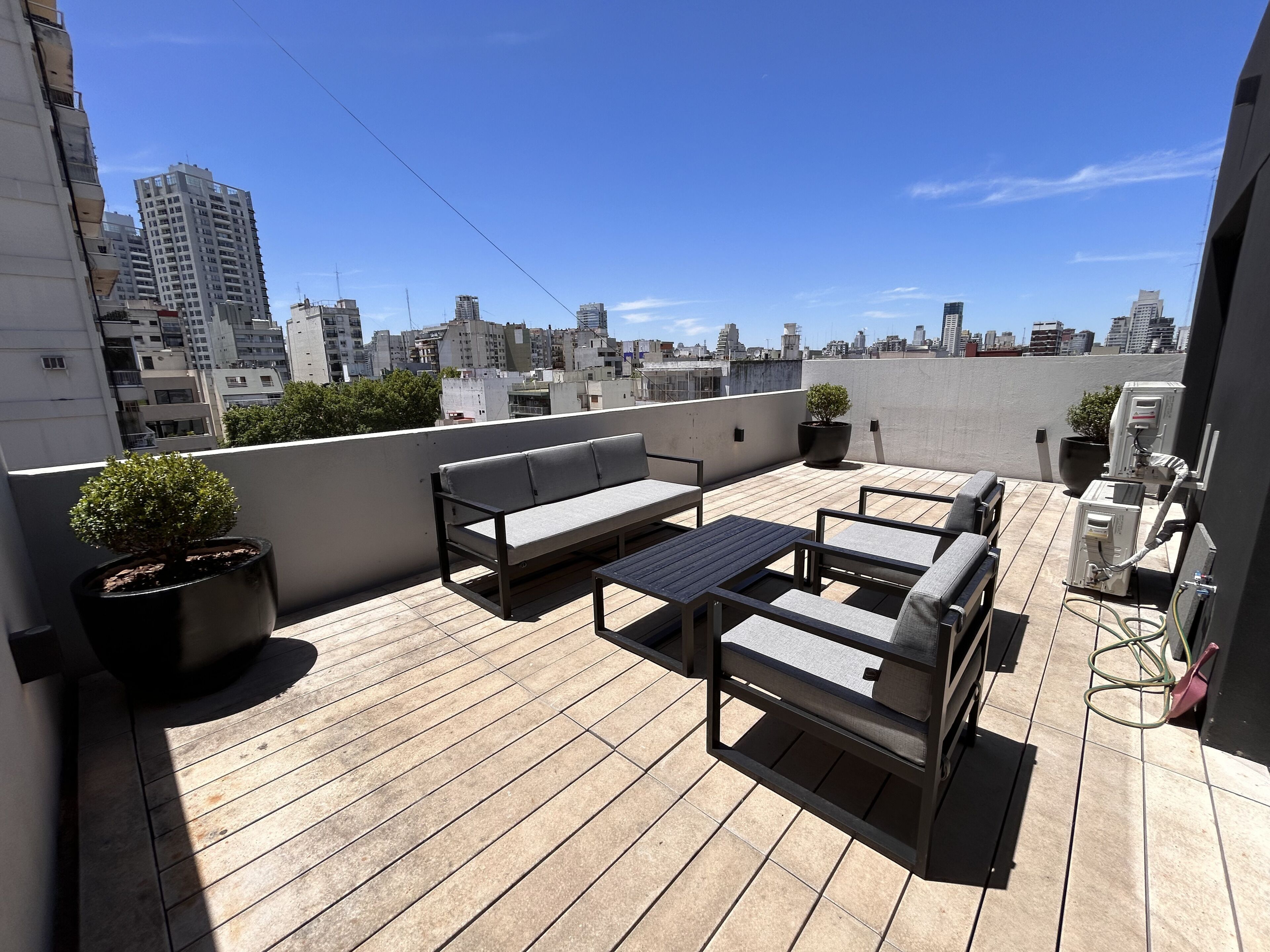 Terraza en la azotea con un conjunto de sofás, una mesita y plantas en macetas.