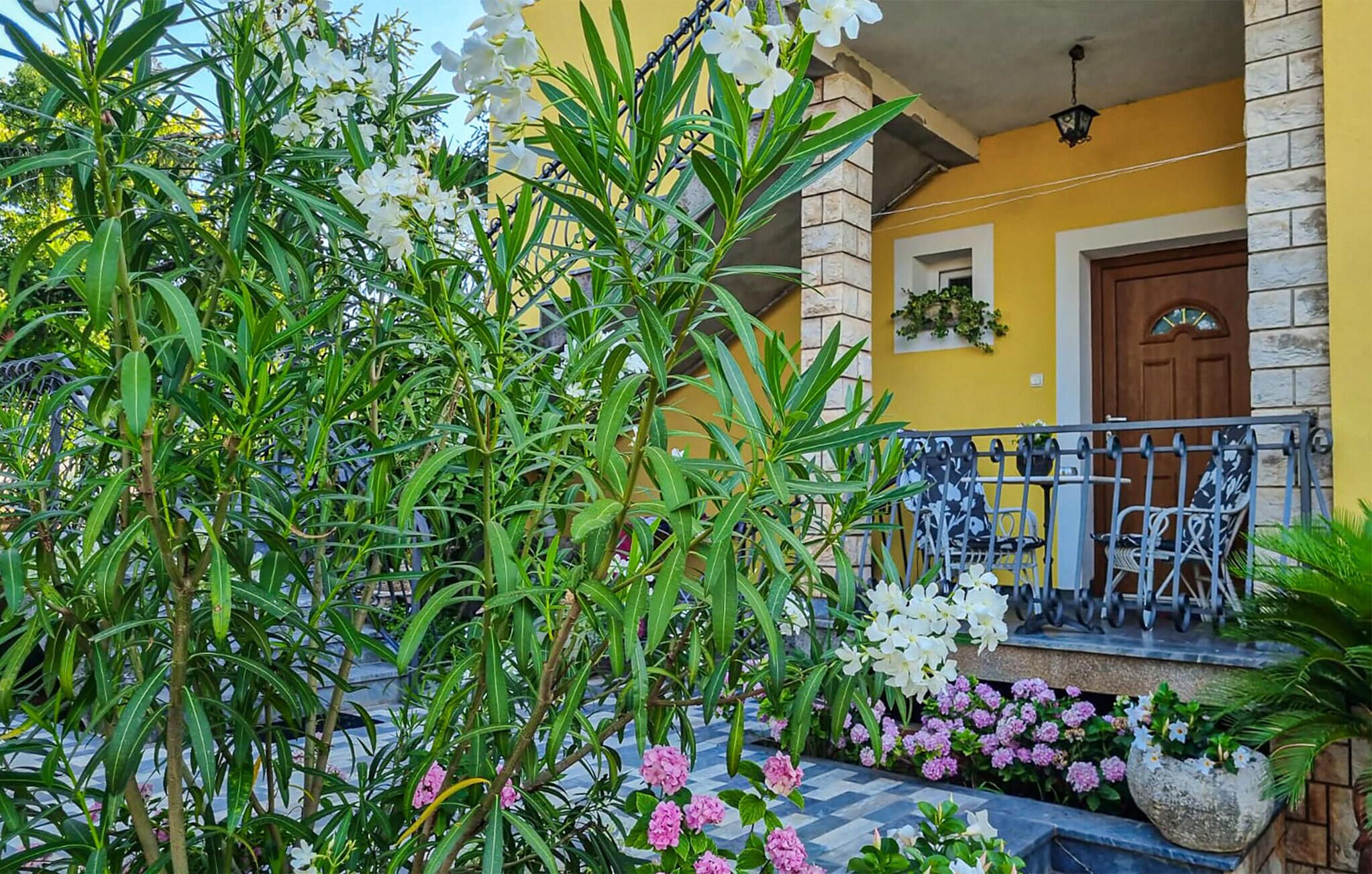 A yellow building with a balcony, surrounded by green plants and flowers.
