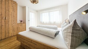 Une chambre à coucher avec une armoire en bois, un lit avec du linge de lit blanc et une tête de lit grise.