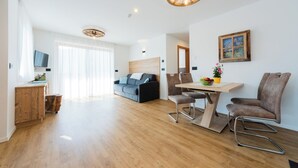 Un salon moderne avec un plancher en bois, un canapé, une table à manger avec des chaises et un téléviseur fixé au mur.