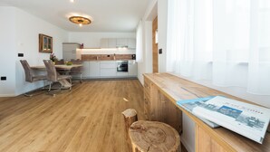 Une cuisine moderne avec des meubles blancs, une table à manger en bois et un four encastré.