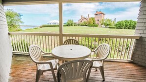 A covered patio with a table and chairs, overlooking a grassy area with a building and a tower. - Oceancliff Resort I & II (Newport)