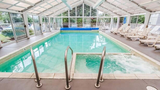 An indoor swimming pool with clear water, a blue deck area, and multiple lounge chairs around the pool. - Oceancliff Resort I & II (Newport)