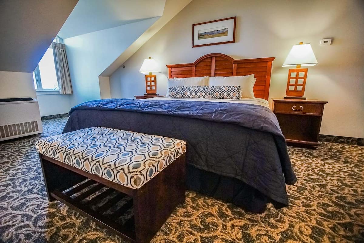 A hotel room with a bed, two bedside tables with lamps, a bench, and a picture on the wall.