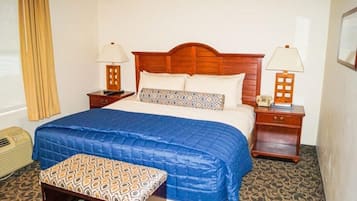A hotel room with a wooden headboard bed, two bedside tables with lamps, a patterned bench, and a radiator.