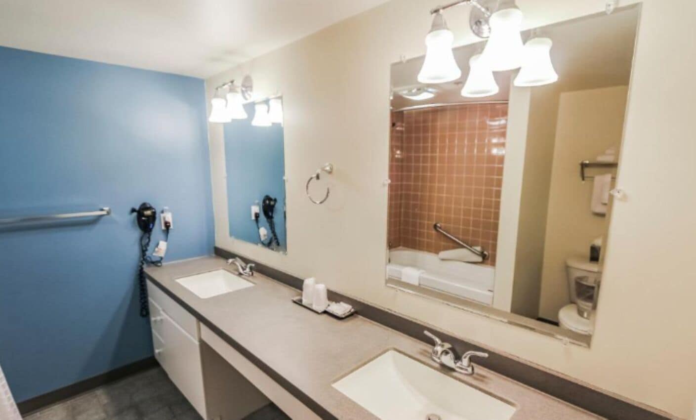 A bathroom with two sinks, a mirror, and a shower area.