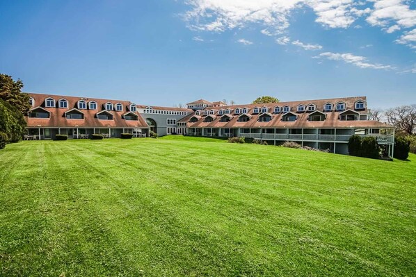 A large, multi-story building with a symmetrical facade, multiple balconies, and a well-maintained lawn in front. - Oceancliff Resort I & II (Newport)