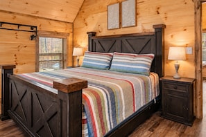 A wooden cabin bedroom with a bed, two bedside lamps, and a window with a view.
