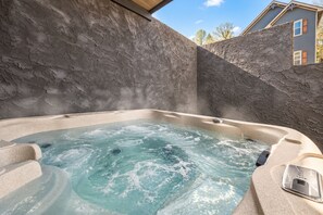 A hot tub with a stone wall backdrop, a control panel, and a clear sky.