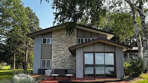 A modern two-story house with a stone facade, large sliding glass doors, and a patio area with outdoor furniture. - Lake Home perfect for families in a quiet Lake Antoine neighborhood.  (Iron Mountain)