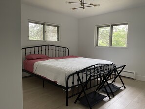 A bedroom with a bed, two windows, a ceiling light fixture, and a radiator.
