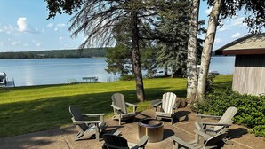 An outdoor seating area with Adirondack chairs and a fire pit, overlooking a lake. - Lake Home perfect for families in a quiet Lake Antoine neighborhood.  (Iron Mountain)
