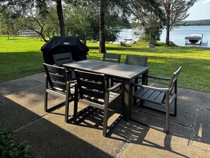 An outdoor patio with a table and chairs, a grill, and a view of a lake.