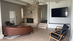 A modern living room with a stone fireplace, leather sofa, and wooden chairs. - Lake Home perfect for families in a quiet Lake Antoine neighborhood.  (Iron Mountain)