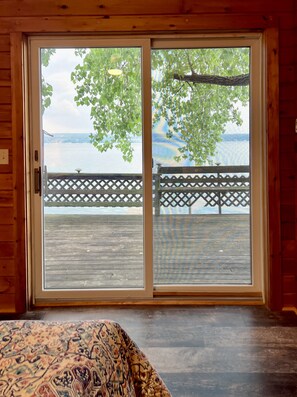 A room with a large sliding glass door leading to a wooden deck overlooking a body of water. - Lakefront, SUPs+kayaks, sunset views & fireplace! Wineries & brewery nearby! ! (King Ferry)