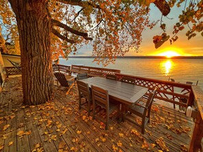 A wooden deck with a table and chairs, overlooking a body of water at sunset. - Lakefront, SUPs+kayaks, sunset views & fireplace! Wineries & brewery nearby! ! (King Ferry)