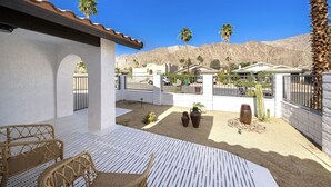 Un espace patio aménagé avec des meubles en osier, un mur blanc et une vue sur un paysage désertique parsemé de palmiers.