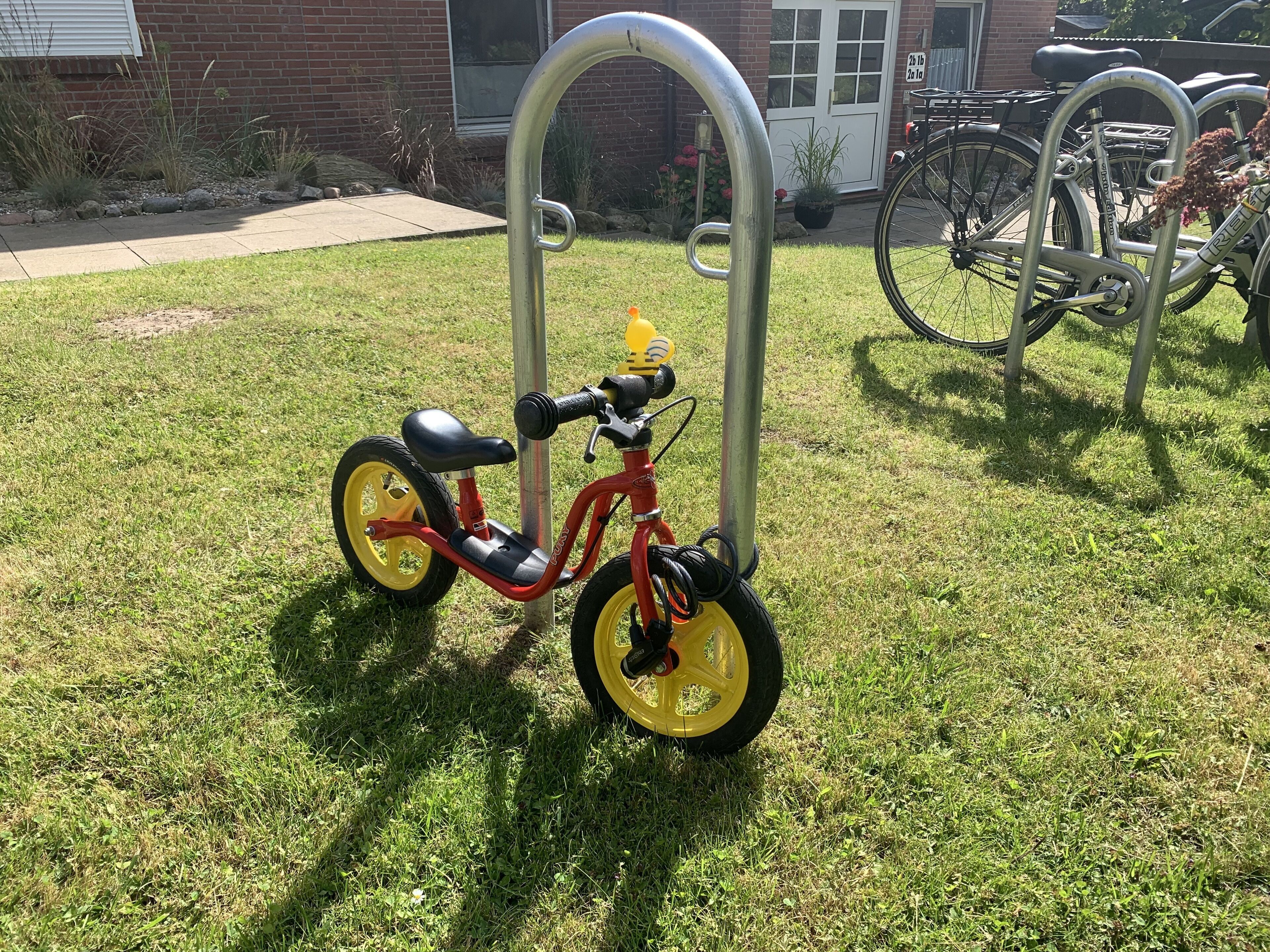 A red children's tricycle parked on a grassy area with a metal bike rack nearby.