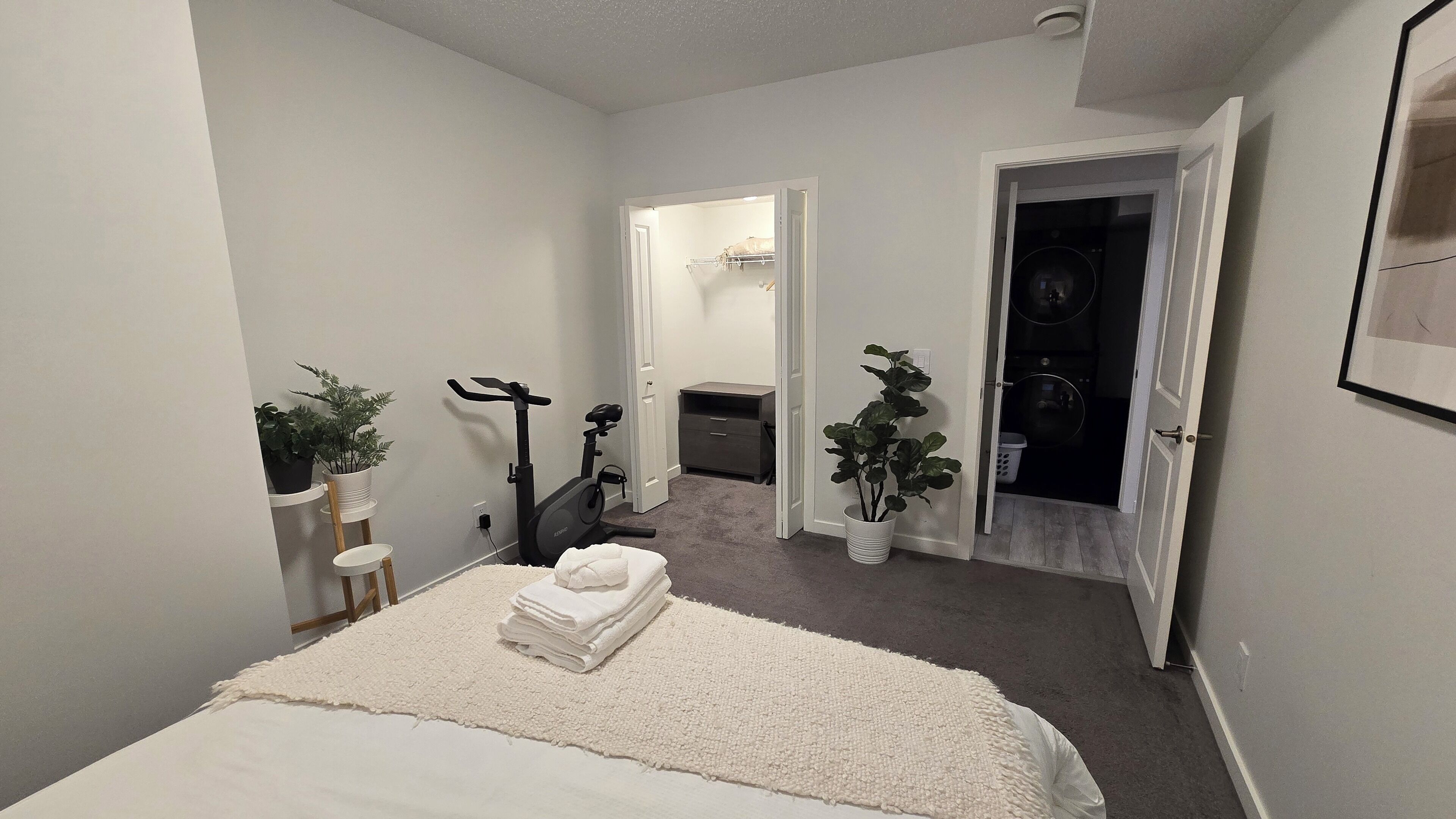 A bedroom with a bed, a treadmill, a small desk, and a closet.