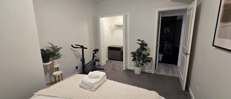 A bedroom with a bed, a treadmill, a small desk, and a closet.