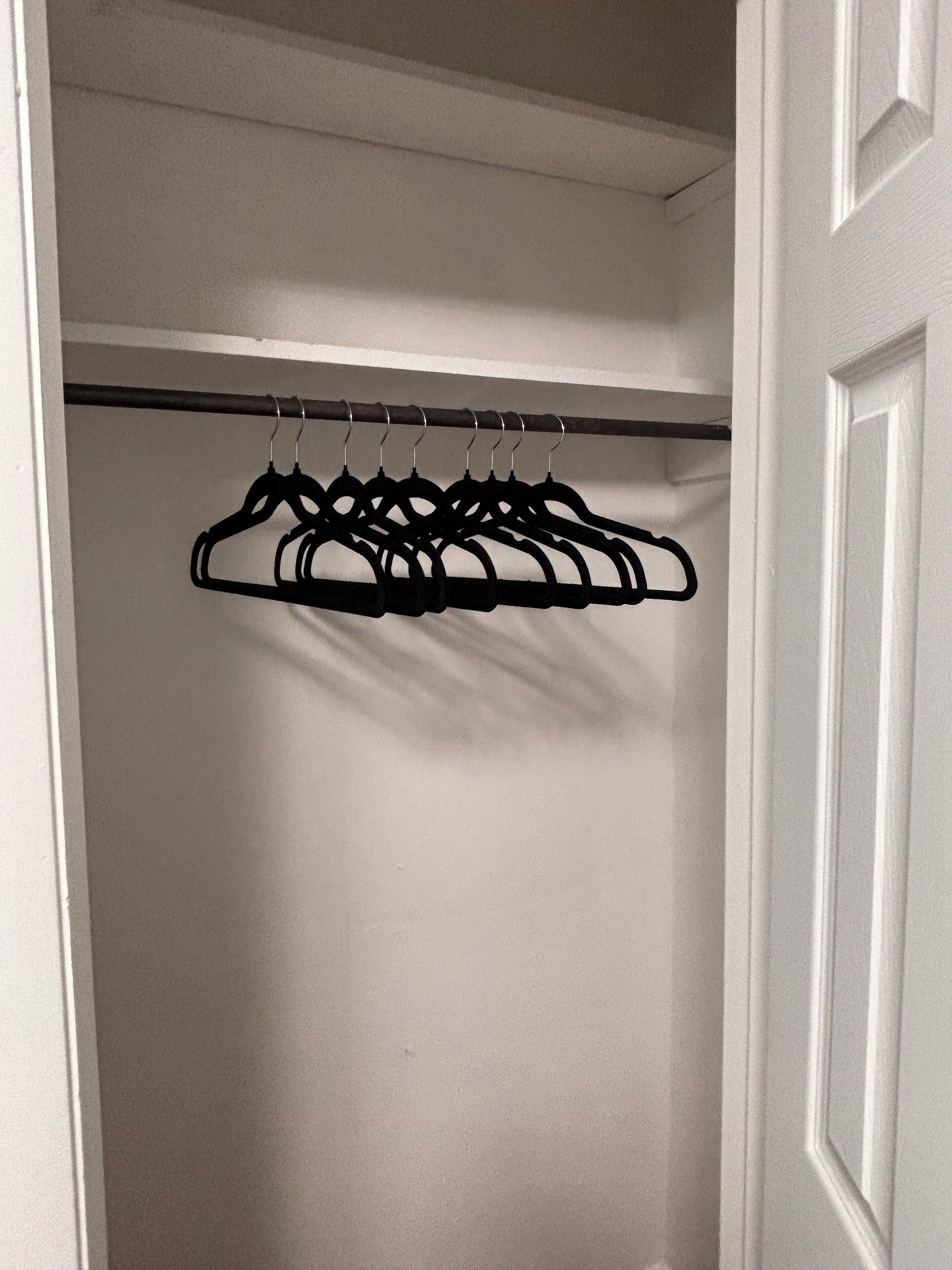 Ein Kleiderschrank mit einer schwarzen Kleiderstange und weißen Wänden.