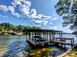 A wooden dock extending into a calm lake, with a covered seating area and a vehicle parked nearby.