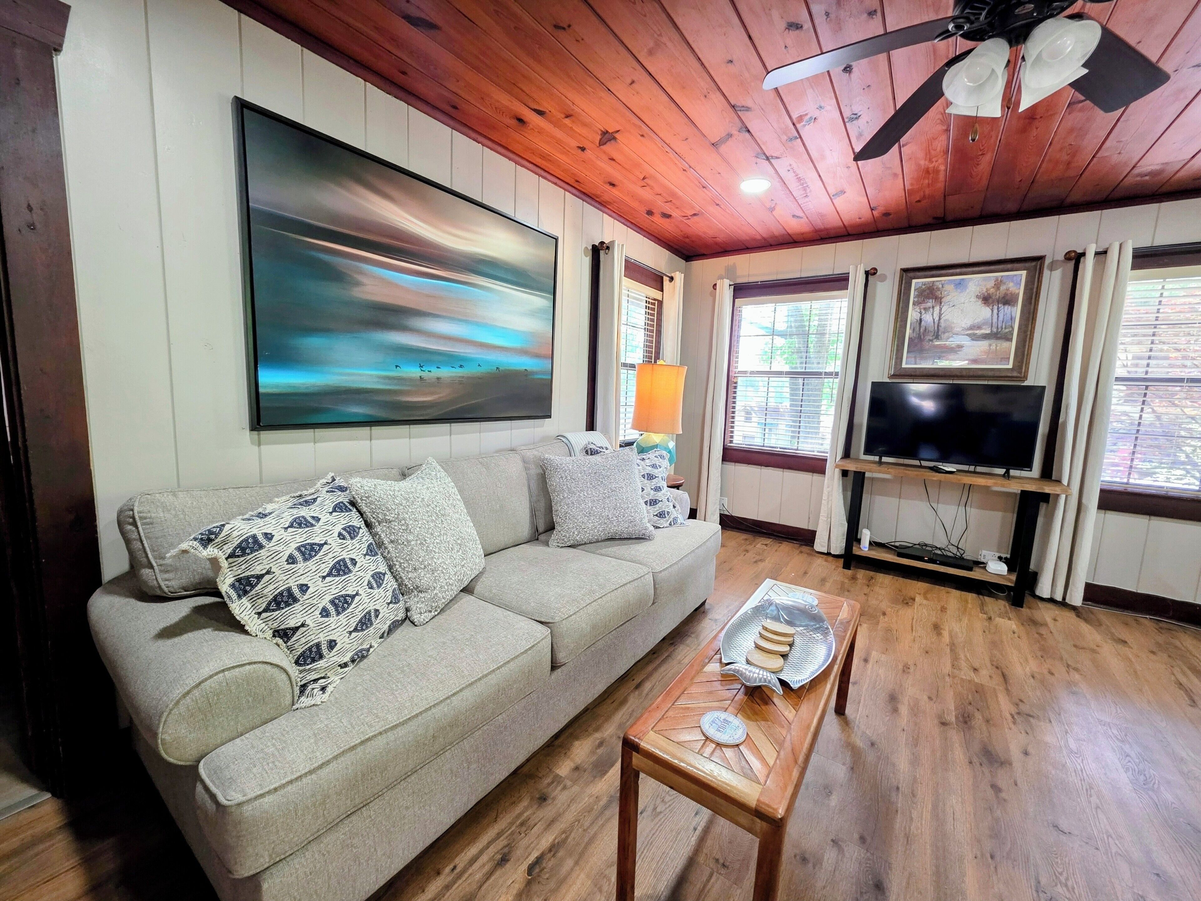 A living room with a sofa, a coffee table, a TV, and a painting on the wall.