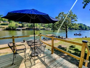A wooden deck with a table and chairs, a blue umbrella, and a view of a lake with boats. - Edgewater Resort (Hot Springs)